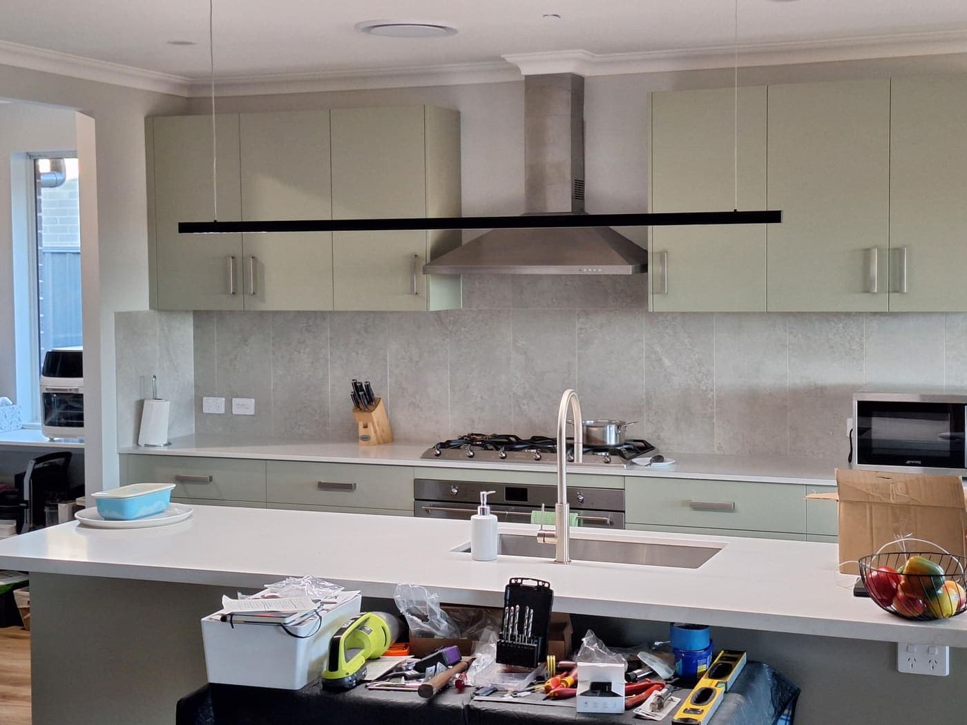 Sage-green kitchen with a linear pendant light, stainless rangehood and gas cooktop