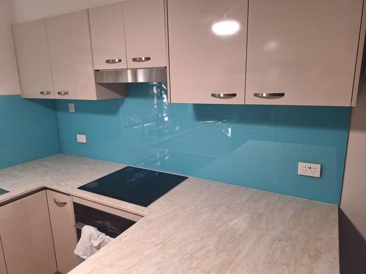 Kitchen with a teal glass splashback, rangehood and induction cooktop