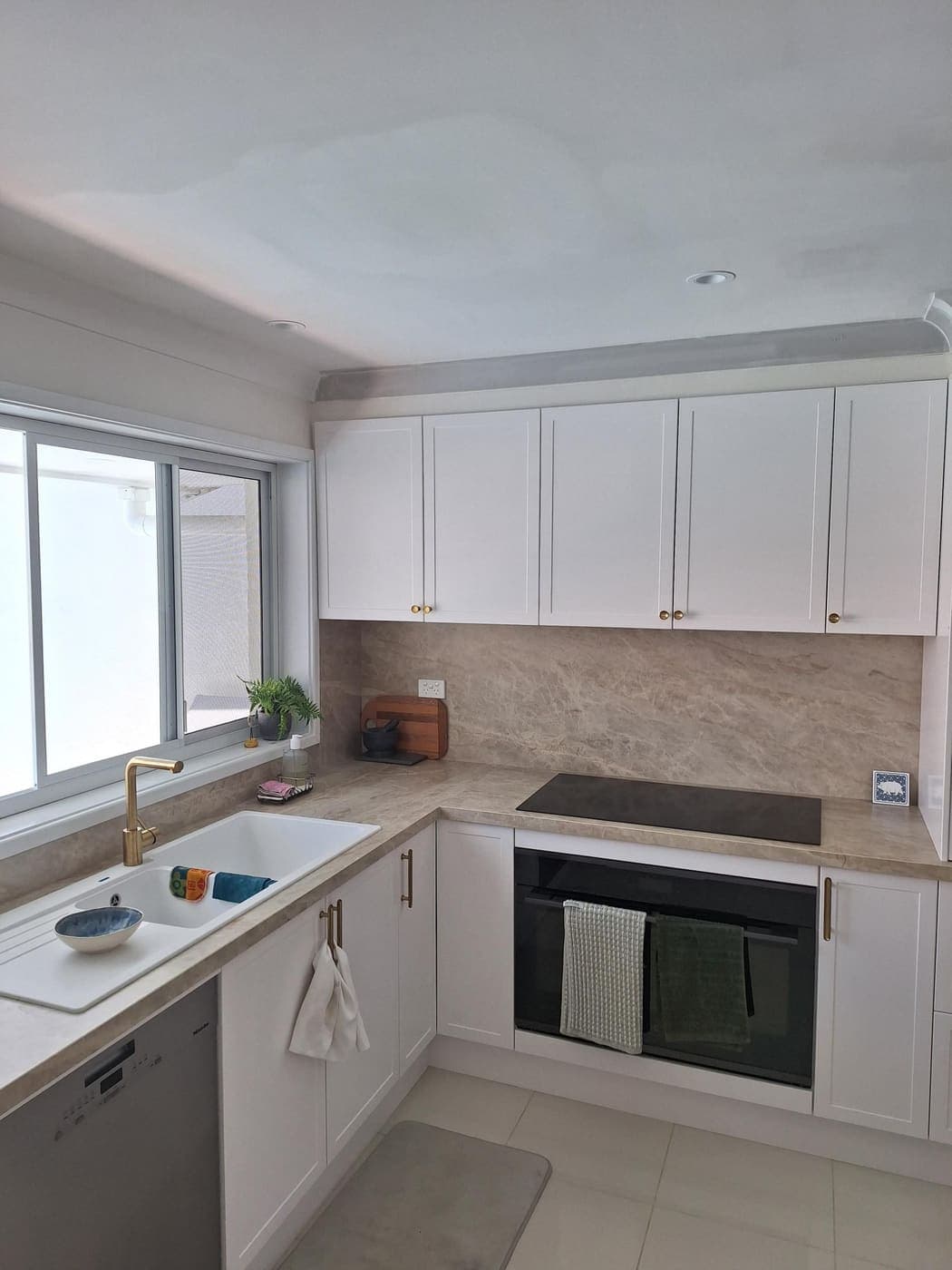 Modern white kitchen with an integrated wall oven, brass handles and stone splashback