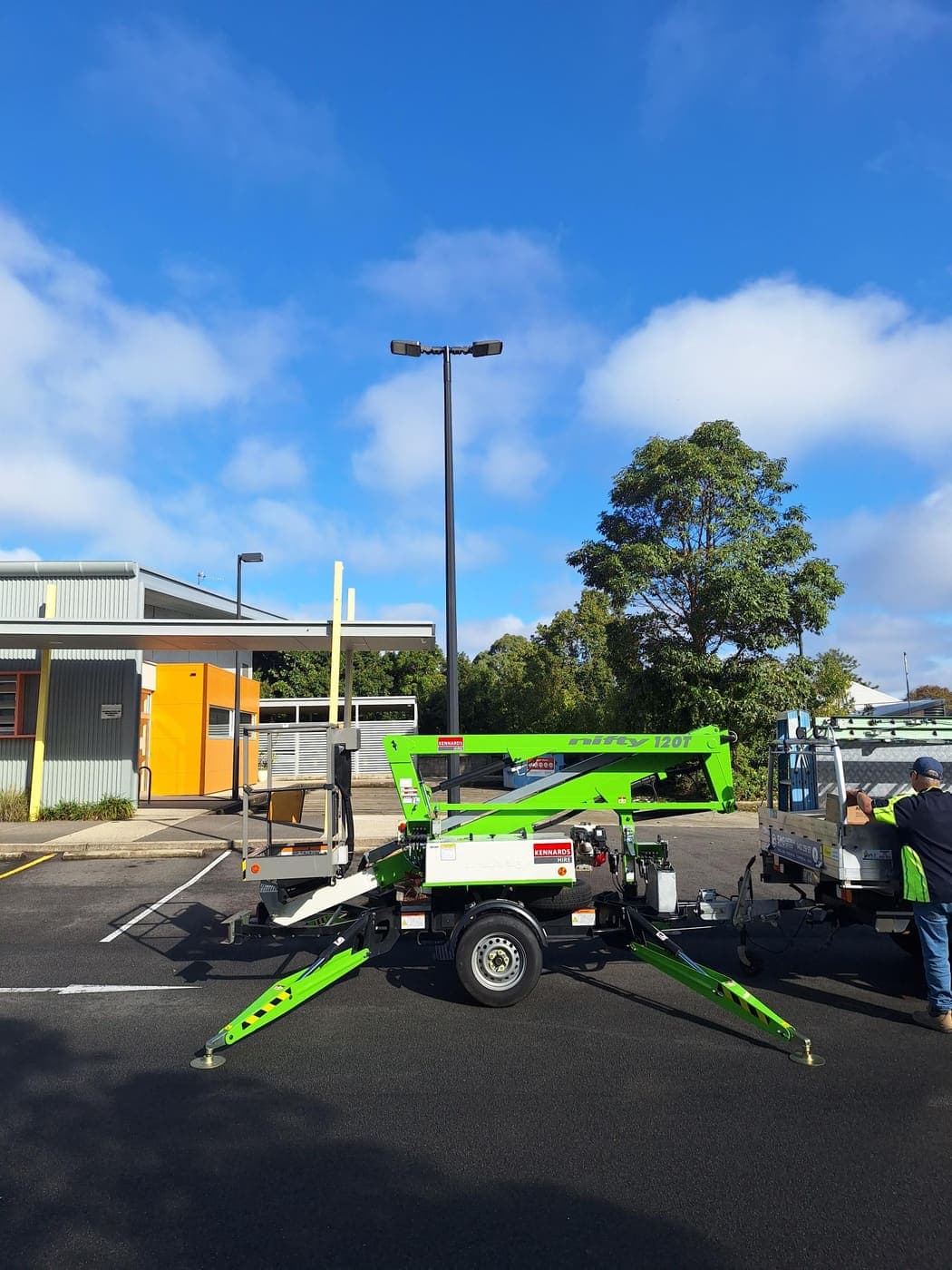 Green Nifty trailer-mounted boom lift set up on a street for high-level work