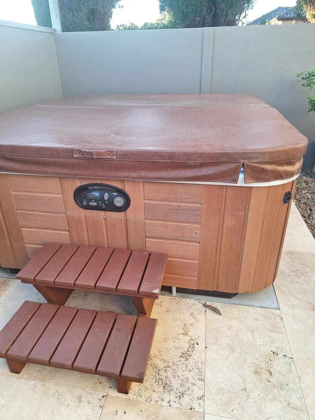Outdoor timber-clad spa with a control panel wired on a paved patio