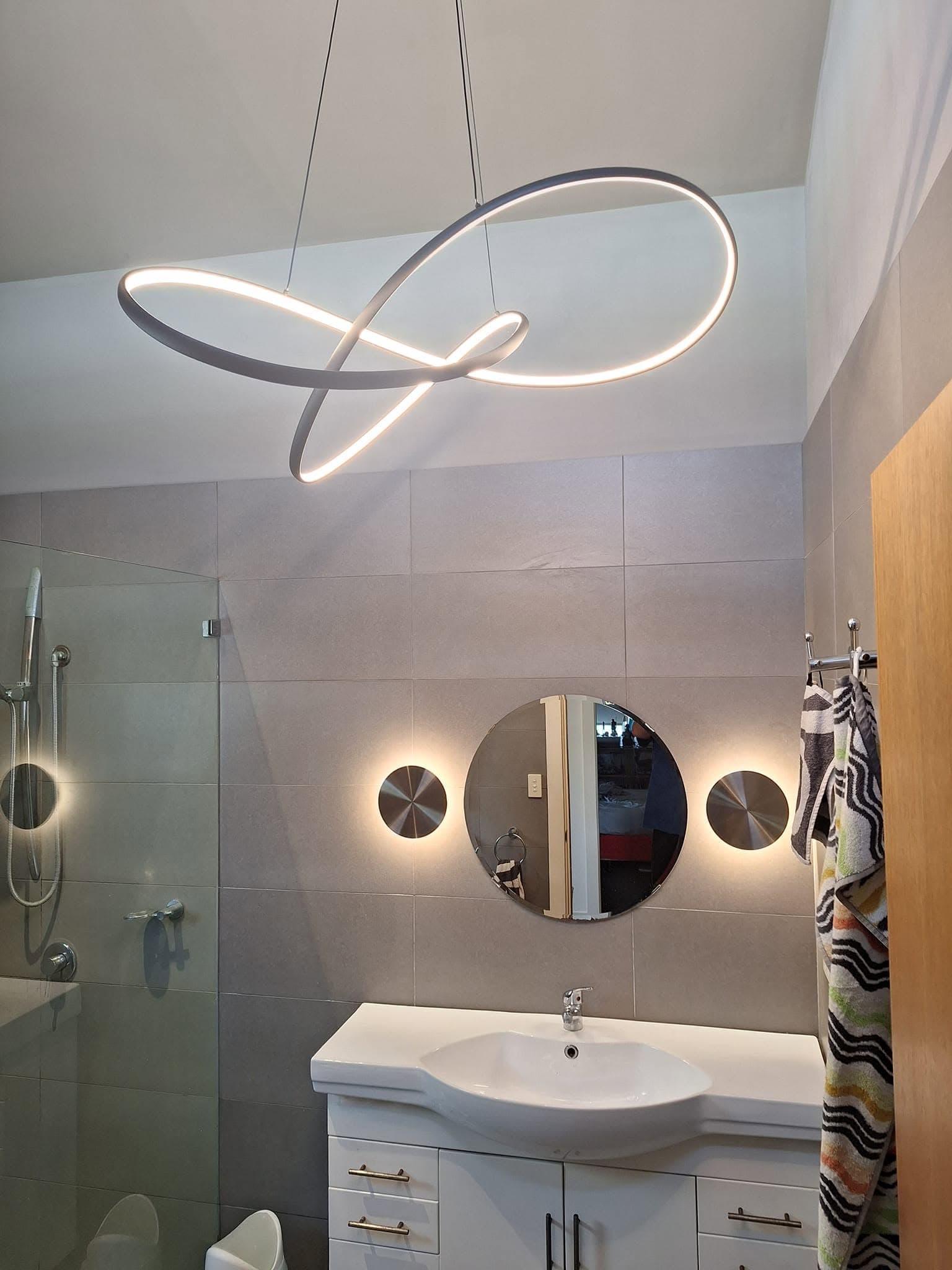Sculptural looped LED pendant light and round wall sconces above a bathroom vanity