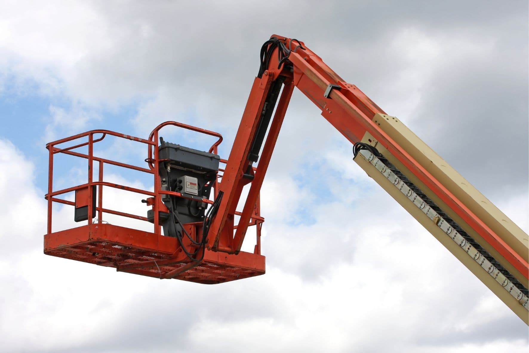 Orange boom lift basket extended high against a cloudy sky for work at heights