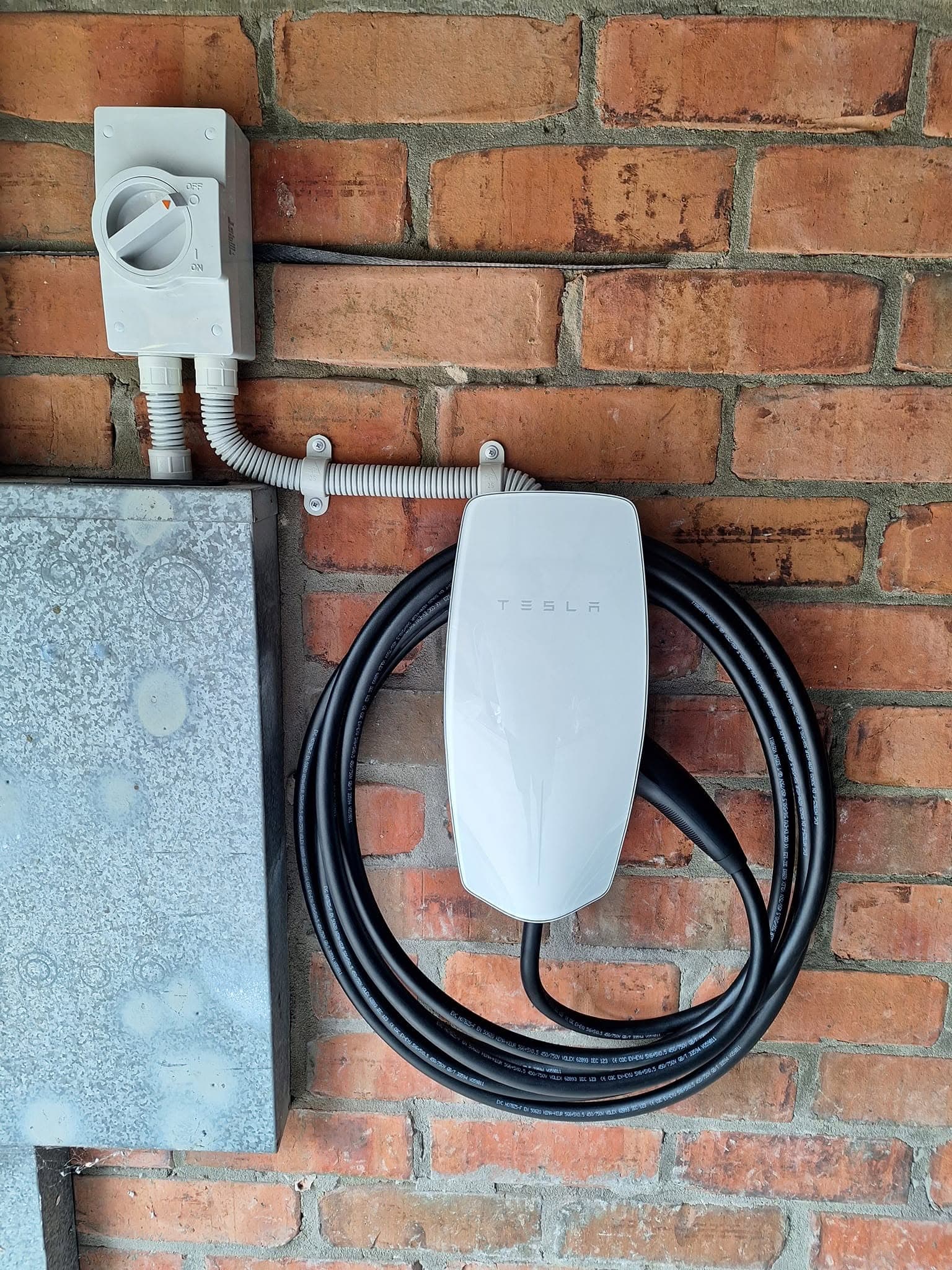 White Tesla wall charger mounted on a brick wall